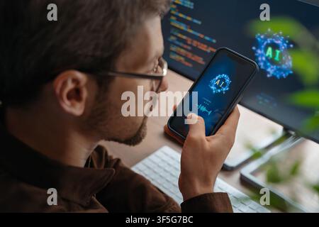 Close up of man holding smartphone talks to an AI powered personal voice assistant using artificial intelligence on phone and computer, interacting with AI chatbot app or giving tasks to an AI agent.  Stock Photo
