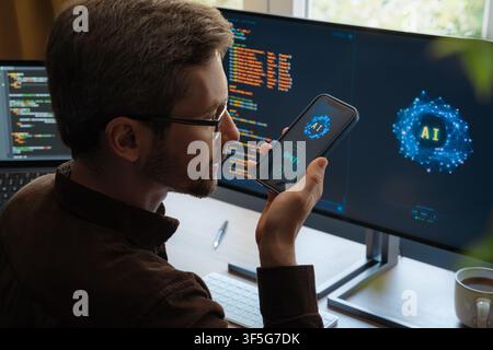 Over-the-shoulder view, of man holding smartphone, talking with AI chatbot app, asking questions, using artificial intelligence assistant for work and daily tasks on phone and computer. Space for text Stock Photo