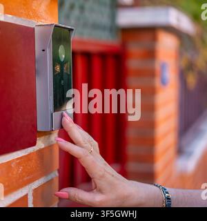 Close view of a woman hand pressing a wall mounted video doorbell beside a residential gate Stock Photo