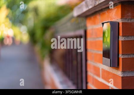Modern video doorbell mounted on an orange brick entrance pillar with blurred street background Stock Photo