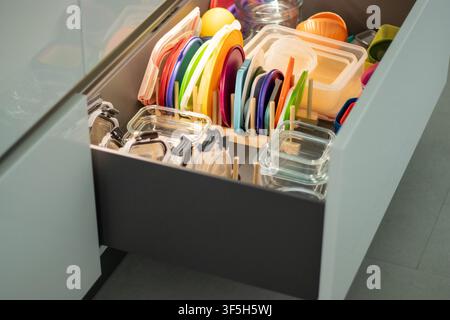 Kitchen drawer filled with colorful plastic lids, glass containers, and various kitchen storage items organized neatly Stock Photo