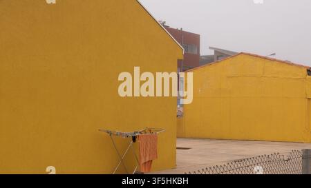 Orange Towel Drying on a Folding Rack Against a Bright Yellow Rendered Wall — Concept: Minimalist Colour Block Composition, Everyday Domestic Life Stock Photo