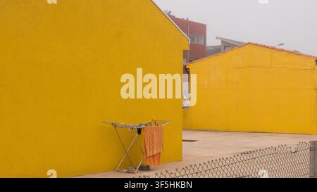 Orange Towel Drying on a Folding Rack Against a Bright Yellow Rendered Wall — Concept: Minimalist Colour Block Composition, Everyday Domestic Life Stock Photo
