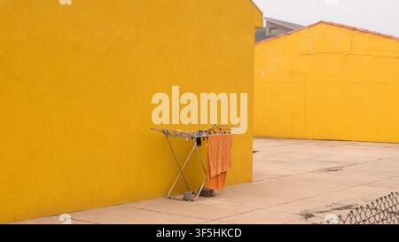 Orange Towel Drying on a Folding Rack Against a Bright Yellow Rendered Wall — Concept: Minimalist Colour Block Composition, Everyday Domestic Life Stock Photo