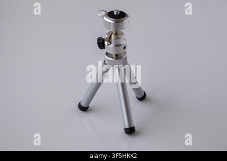 Small silver metallic mini tripod stand placed on plain white surface. Portable tabletop mount accessory for mobile phone and camera support equipment Stock Photo