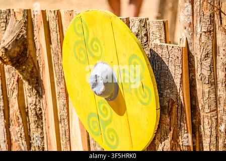 Historical reenactment scene showing a painted round shield mounted on a timber wall in daylight Stock Photo