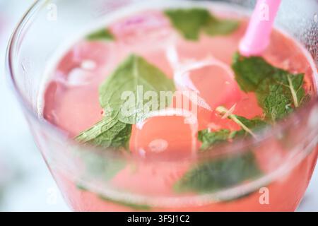 Close-up of cold raspberry lemonade in a glass decorated with ice cubes, green mint leaves, and a pink straw for a refreshing drink. Stock Photo