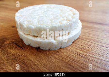 Two rice cakes are stacked on a wooden table. The scene shows a close-up view of these snacks. The background is light and simple, focusing on the ric Stock Photo