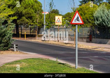 Bicycle warning sign beside an urban road and marked cycle crossing surrounded by trees Stock Photo