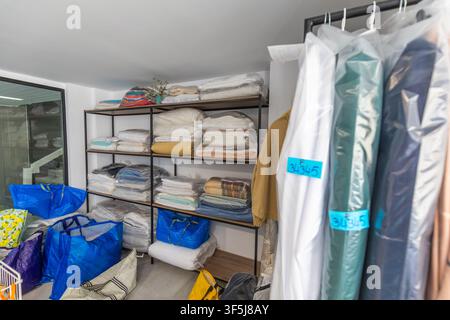 Neat laundry storage room with metal shelving full of folded towels, sheets, and blankets, plus large bags and garments in plastic covers, ready for c Stock Photo