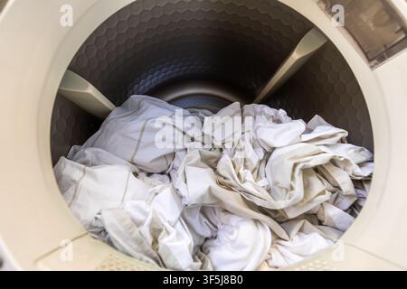 Closeup of crumpled white laundry inside a front load washing machine drum, showing household chores, cleaning routine, fabric care, and home applianc Stock Photo