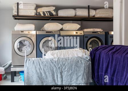 Contemporary laundry room with washer and dryer units, baskets and hanging clothes, plus neatly folded towels and bedding on open shelving for organiz Stock Photo