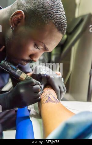 Close-up of a professional tattoo artist wearing gloves, carefully tattooing a detailed line work design on a client's instep foot in a modern studio, Stock Photo