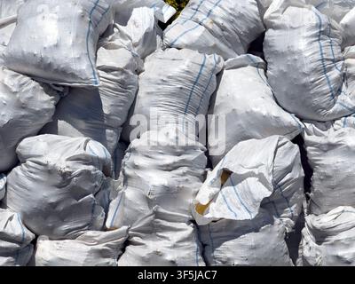 Close-up of stacked white woven sacks filled with construction material at a construction site, showing rough fabric texture, blue seams, dust, and in Stock Photo