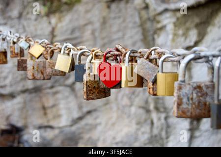 A heart-shaped red padlock stands out among several rusty locks on a chain, symbolizing love and commitment. Captured in Bosnia and Herzegovina, the i Stock Photo
