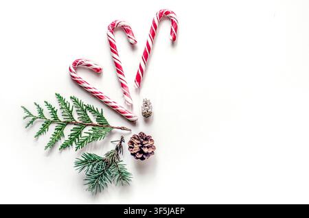 Red and white candy canes arranged beside evergreen sprigs and pine cones on a bright white background, creating a festive Christmas flat lay. Stock Photo