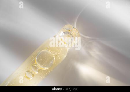 Macro view of a cosmetic pipette filled with translucent golden gel, featuring air bubbles and caustic light reflections on a soft neutral background. Stock Photo