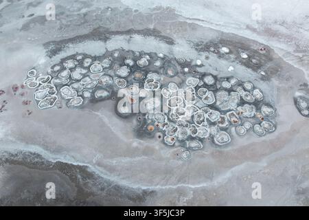 Aerial view of Laguna Espejo showing abstract salt and mineral formations along the shoreline, with pale gray water, textured flats, and organic circu Stock Photo