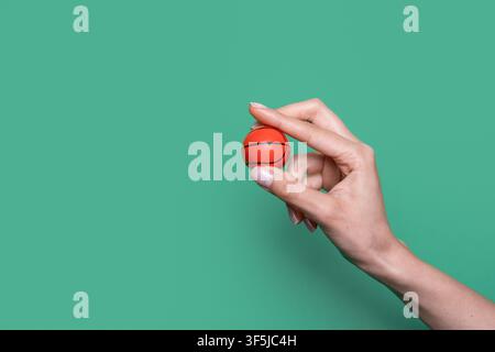 Close-up of a hand delicately holding a miniature orange basketball between fingers against a clean turquoise green background with generous copy spac Stock Photo