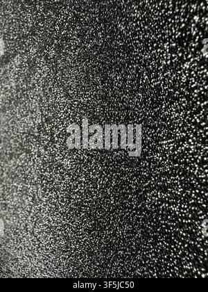 Abstract close-up of a black textured surface covered with fine shimmering silver speckles. The dark grainy background creates a dramatic metallic pat Stock Photo