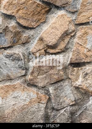 Close-up of a rough natural stone wall with irregular beige and gray rocks set in textured mortar, creating a durable rustic masonry surface and archi Stock Photo