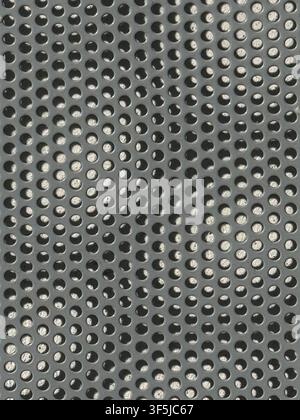 Abstract close-up texture of a gray perforated metal sheet, featuring an orderly grid of circular holes, metallic reflections, shadows, and an industr Stock Photo