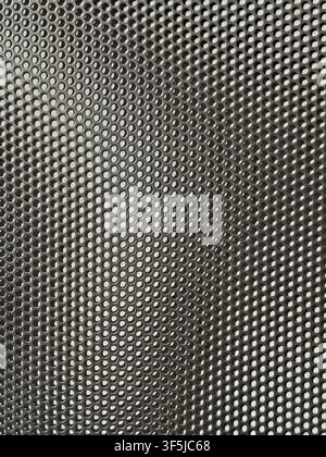 Close-up abstract view of silver perforated metal mesh with repeating circular holes, creating an industrial geometric texture, detailed surface patte Stock Photo