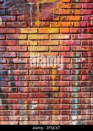 Close-up of a weathered red brick wall covered with colorful graffiti paint, drips, splashes, and layered urban marks, creating a vibrant abstract gru Stock Photo