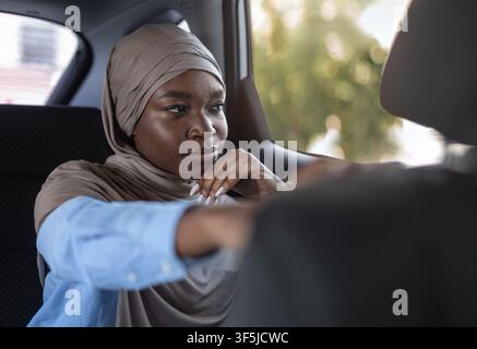 Confident black muslim businesswoman sitting in car and looking through window Stock Photo