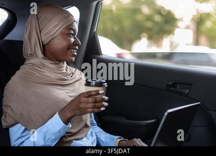 Cheerful Black Muslim Lady In Hijab Drinking Takeaway Coffee In Car Stock Photo