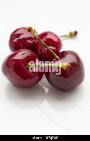 Close-up of ripe sweet cherries isolated on a white background. Glossy red fruits with green stems arranged in a simple composition Stock Photo