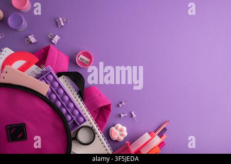 A vibrant pink backpack overflowing with assorted school supplies such as notebooks, pens, a pop-it fidget toy, a protractor, binder clips, and a penc Stock Photo