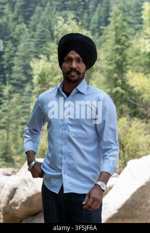 A three-quarter portrait of an Indian Sikh man wearing a traditional black turban, a light blue pinstriped long-sleeve button-down shirt. Stock Photo
