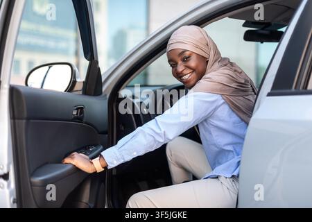 New Car. Happy black muslim businesswoman getting in luxury auto and smiling Stock Photo