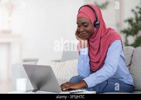 Positive black muslim lady watching webinar on laptop, studying at home Stock Photo