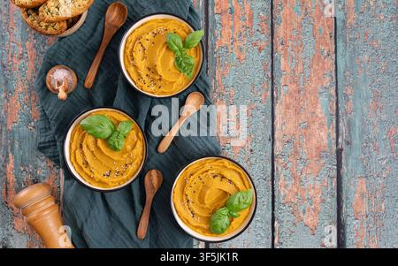 Homemade pumpkin soup garnished with basil served with slices of rustic bread on a wooden table Stock Photo