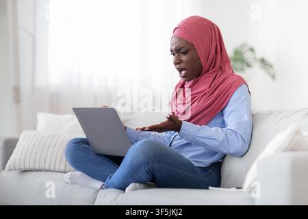 Computer problems. Angry arab woman having issues with laptop at home, annoyed of bad internet connection, free space Stock Photo