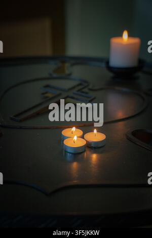 Three burning tealight candles beside a Christian cross in a dark church interior Stock Photo