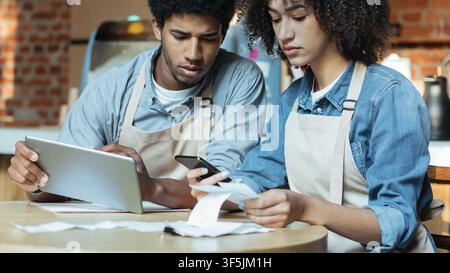 Concentrated professional administrative managers of coffee shop make revisions after working day using tablet Stock Photo