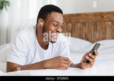 Joyful African Guy Making Video Call On Smartphone In Bedroom Stock Photo