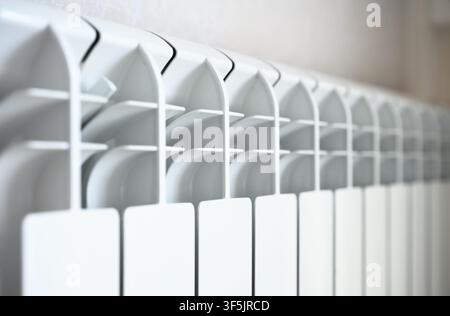 A close-up photograph of a modern white central heating radiator mounted on a light-colored wall. The image features a shallow depth of field, focusin Stock Photo