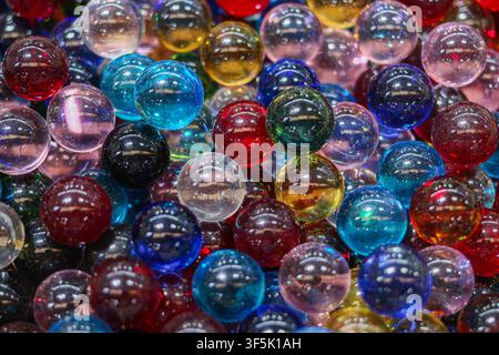 Close up of colorful transparent glass marbles forming a glossy abstract background with overlapping spherical shapes and reflections. Stock Photo