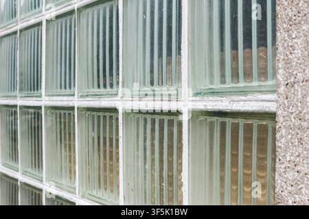 Diagonal close-up of weathered translucent glass block wall with white grout beside a concrete facade texture. Stock Photo