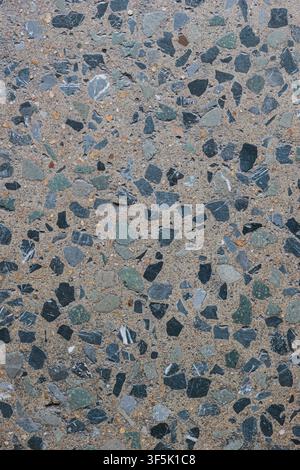 Top view vertical outdoor cool grey terrazzo surface. Weather resistant composite material with black, white, green, and orange stone chips. Stock Photo