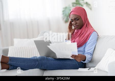 Black Muslim Lady Having Headache While Working Remotely With Papers At Home Stock Photo