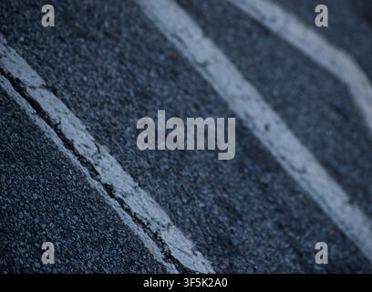 Close-up footage of weathered white lane markings on an asphalt road with shallow depth of field. For transportation, road safety, infrastructure Stock Photo