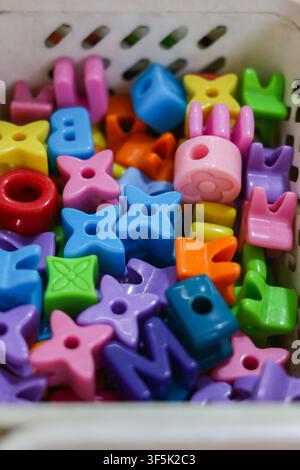 Colorful alphabet and star shaped plastic beads stored in a container for children's crafts, creative play, letter learning and educational activities Stock Photo