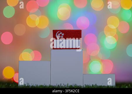 Embroidered Singapore flag on the highest block of a white winner podium against a colorful bokeh background, depicting first place. Stock Photo