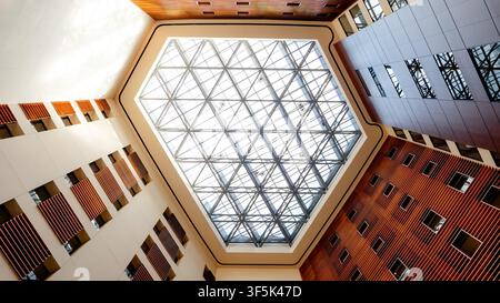 Upward view of a modern atrium in Minato, Tokyo, featuring a geometric glass skylight roof, clean lines, warm wood panels, and contemporary urban arch Stock Photo