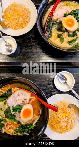 Top view of Japanese ramen noodles with pork and soft boiled egg, served with fried rice on a black tray. Restaurant meal set with spoons. Stock Photo